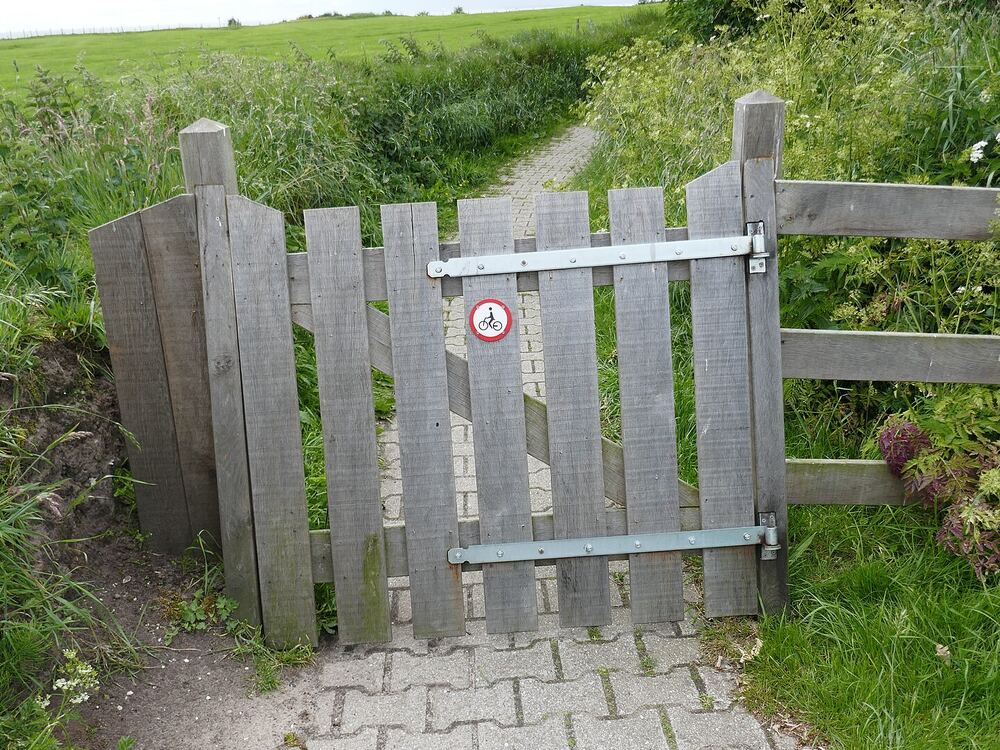 Houten klaphek over een smal wandelpad door groen weiland bij Oudemirdum